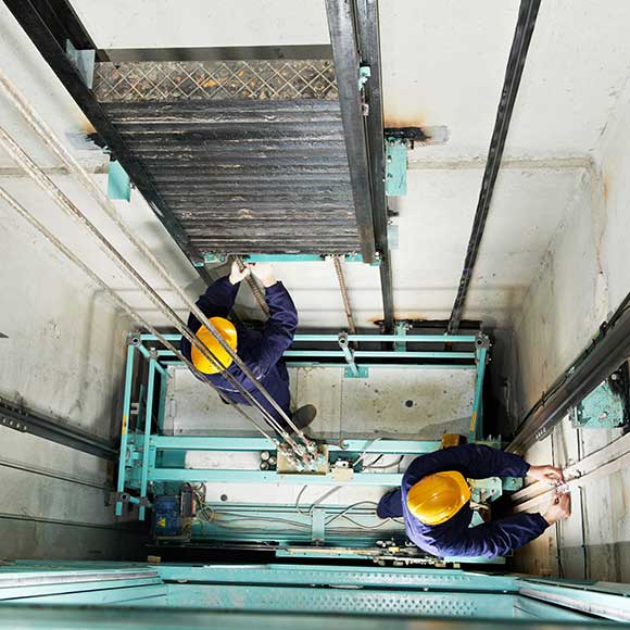 Two men working on lift to promote Greenfield Risk Solutions Insurance Brokers - Specialist Risk and Contractor Insurance - Lift Engineers